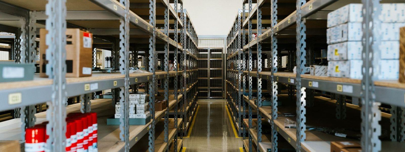 Aisle of used industrial steel clip shelving stocked with boxed parts in a warehouse